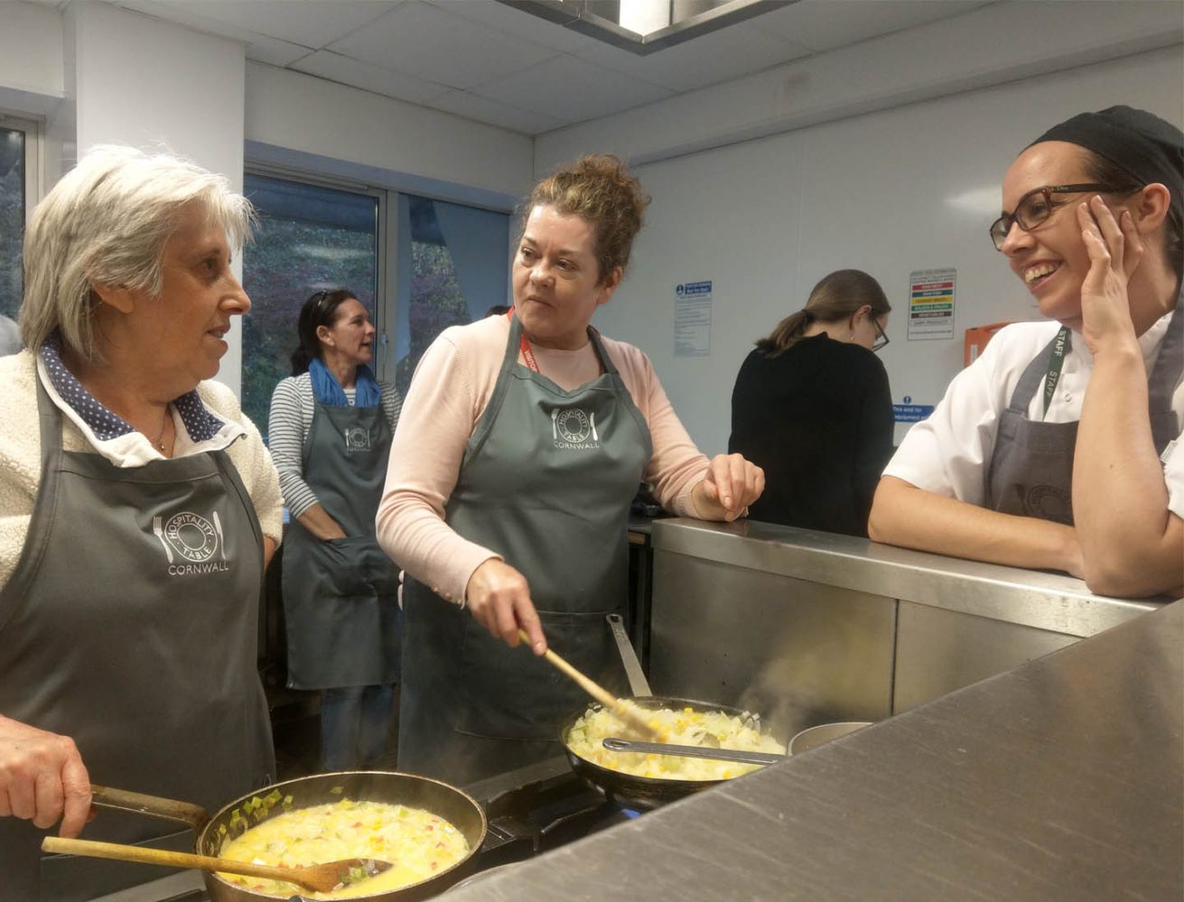 A picture of 3 ladies in aprons preparing food and chatting